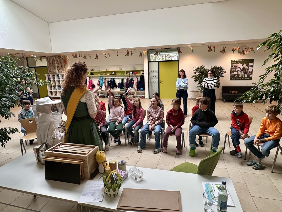 Eine Gruppe von Kindern hört einer Lehrerin und einer Imkerin im Klassenzimmer zu.