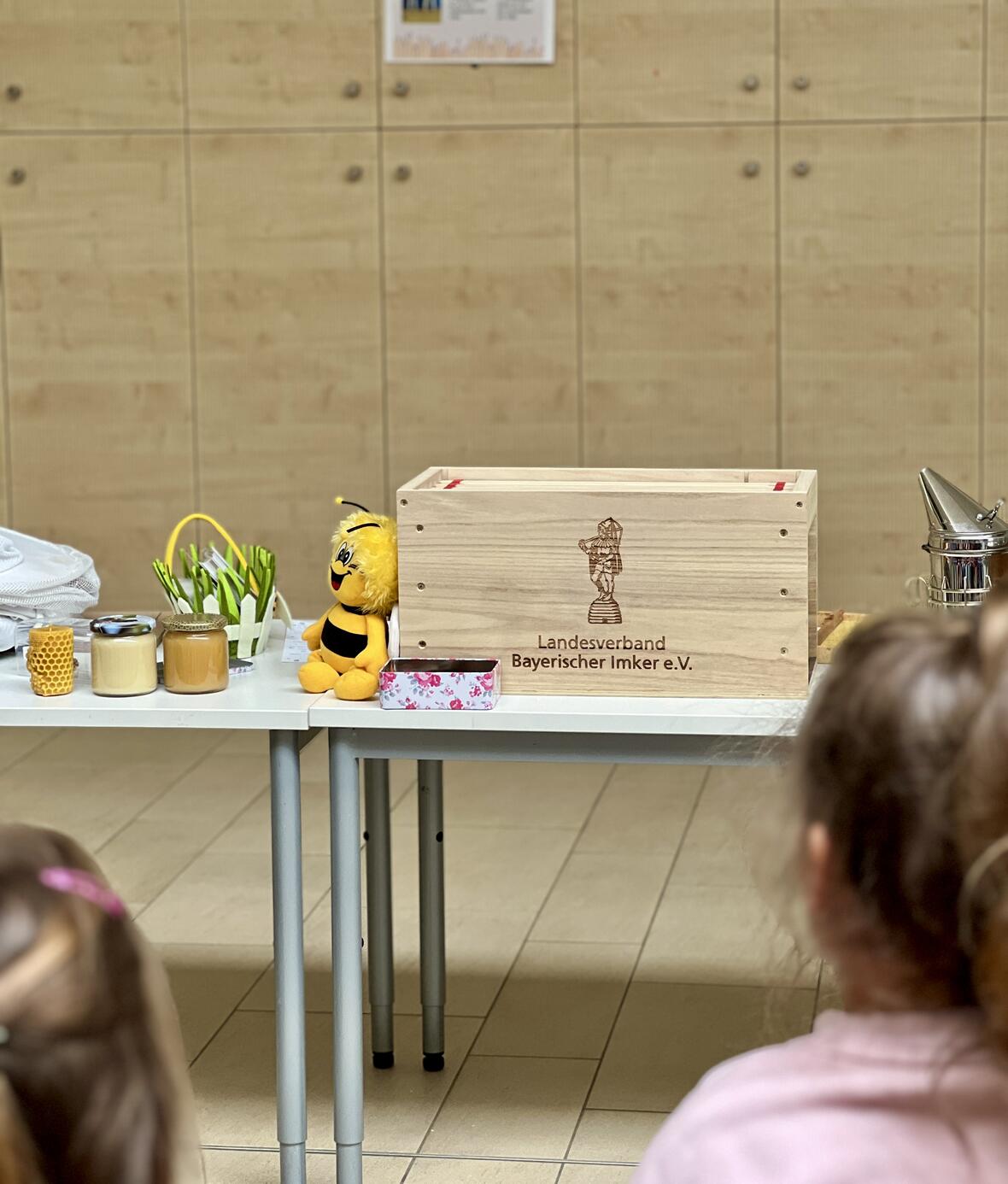 Holzkiste des Landesverbands Bayerischer Imker mit Honig und einer Biene aus Plüsch, Blick auf Kinder.