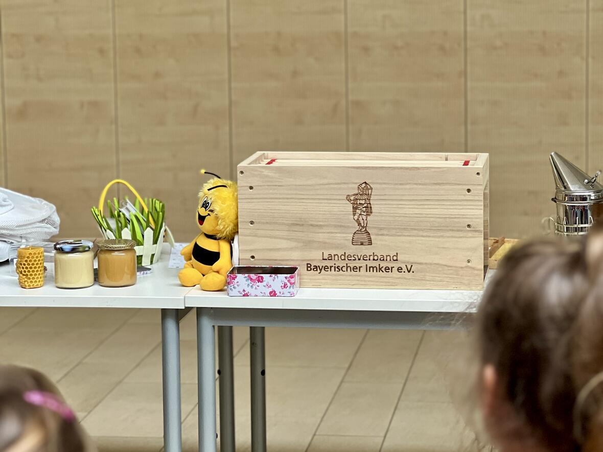 Holzkiste des Landesverbands Bayerischer Imker mit Honig und einer Biene aus Plüsch, Blick auf Kinder.