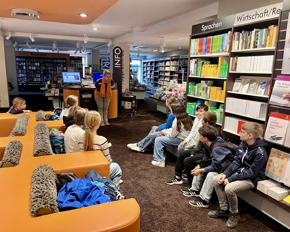 Eine Frau erklärt einer Gruppe von Schülern in einer Bibliothek die Buchauswahl.