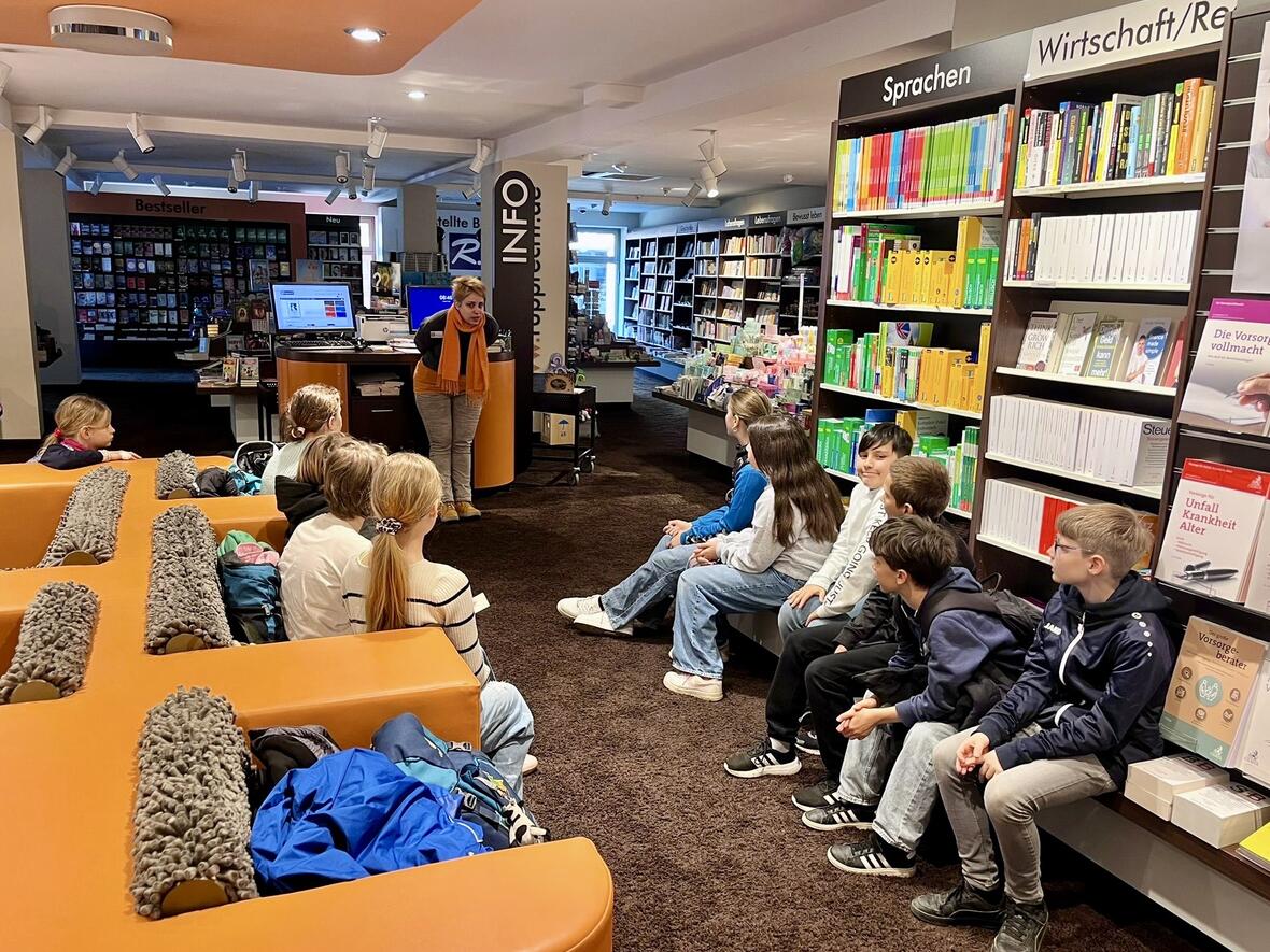 Eine Frau erklärt einer Gruppe von Schülern in einer Bibliothek die Buchauswahl.