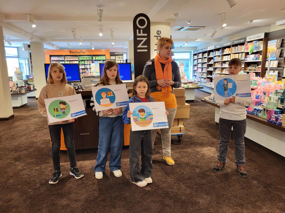 Vier Kinder mit Schildern, die verschiedene Berufe vorstellen, stehen in einem Buchladen.