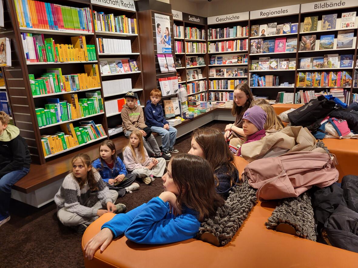 Gruppe von Kindern sitzt auf einem Sofa in einer Buchhandlung, umgeben von Bücherregalen.
