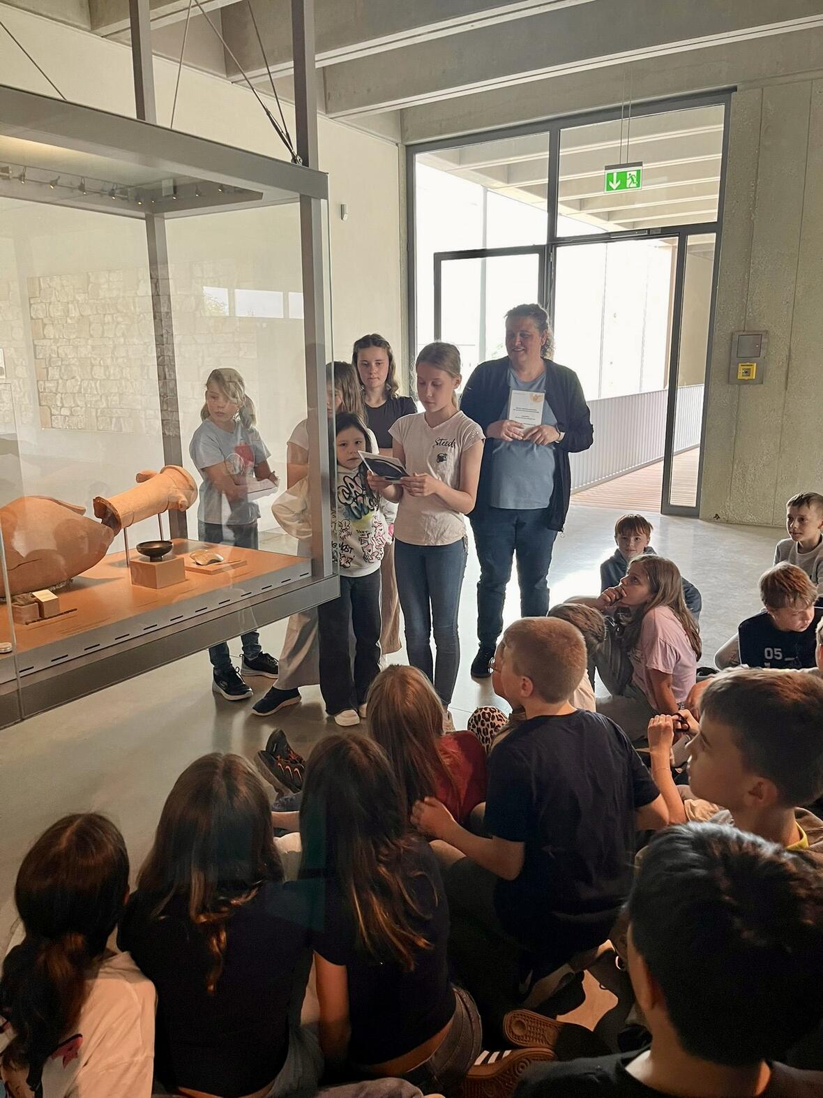Kinder hören einer Erklärung zu einem archäologischen Fund in einem Museum.