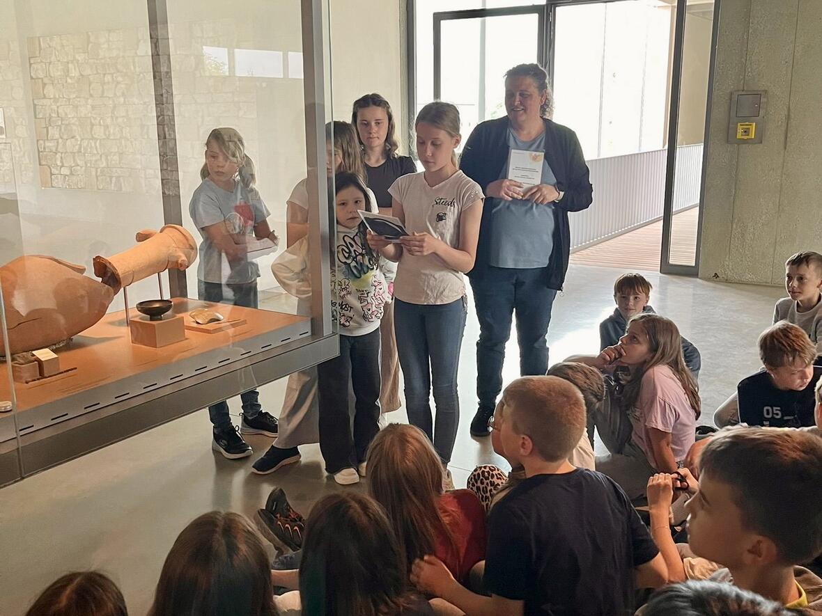 Kinder hören einer Erklärung zu einem archäologischen Fund in einem Museum.