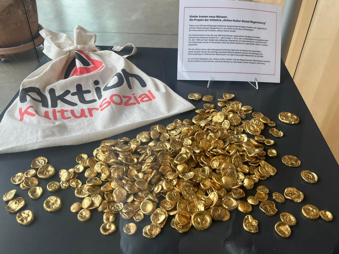 Goldfarbene Münzen und ein Stoffbeutel der Aktion Kultursozial in Regensburg.