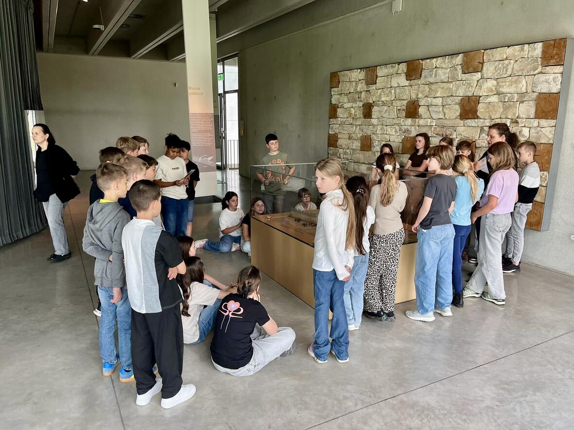 Gruppe von Schülern in einem Museum, versammelt um eine Vitrine mit Ausstellungsstücken.