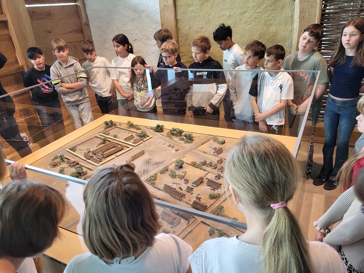 Schulgruppe betrachtet ein Modell einer historischen Siedlung in einem Museum.