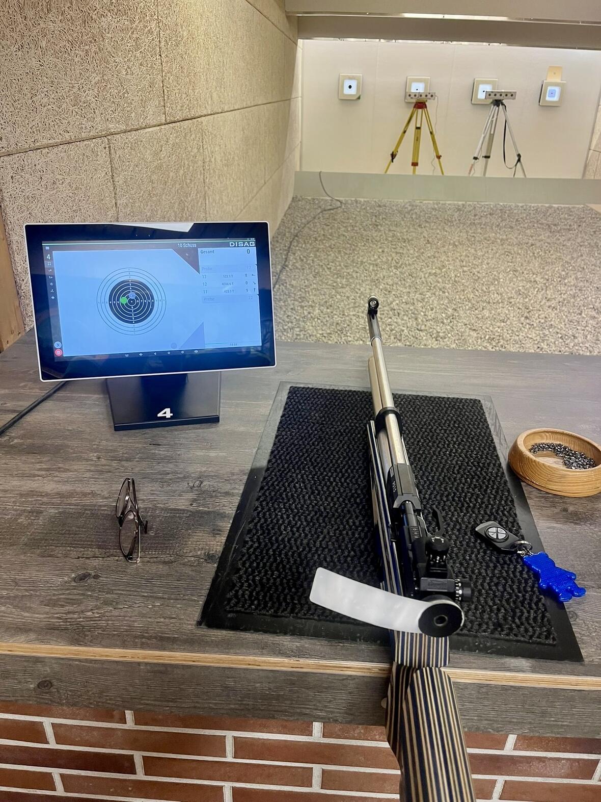Schießstand mit digitaler Zielanzeige, Luftgewehr und Zubehör auf dem Tisch.