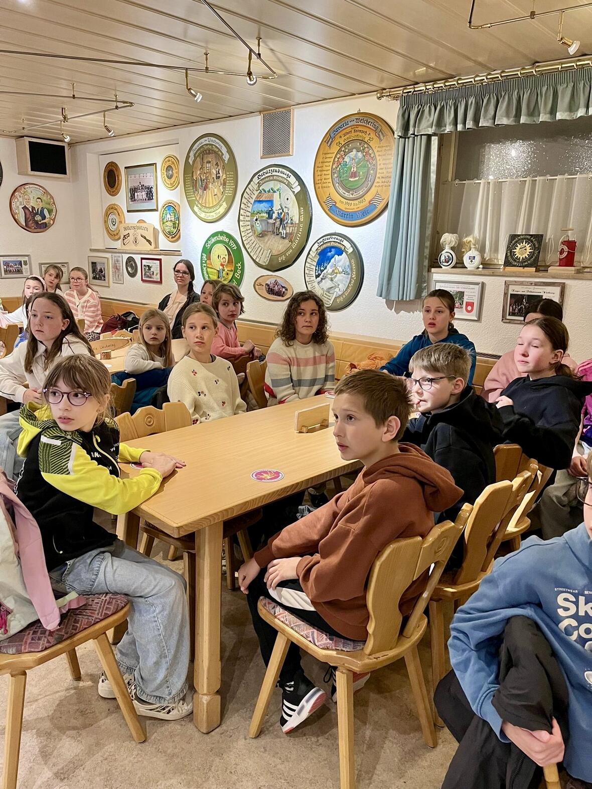 Kinder sitzen an einem Tisch in einem gemütlichen Raum mit Wandbildern und interessiertem Blick.