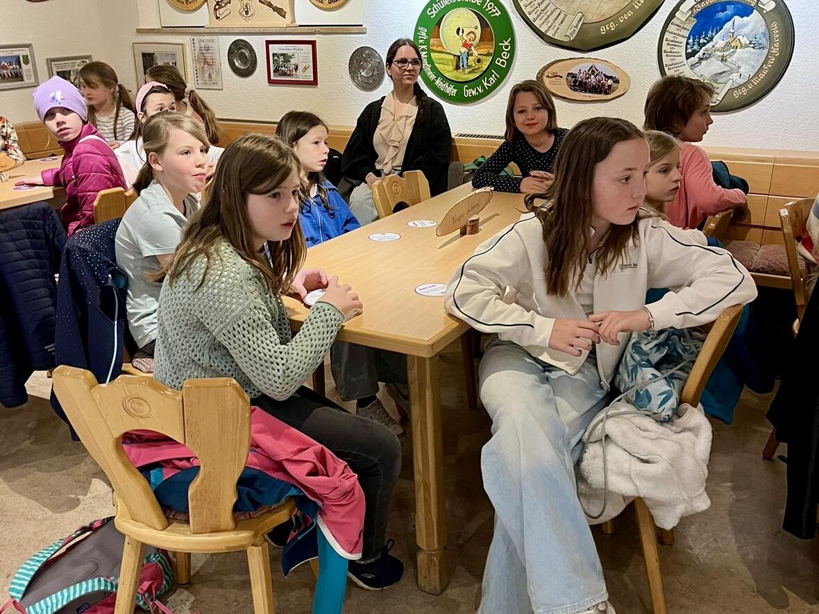 Gruppe von Kindern in einem Raum mit Wanddekorationen, die aufmerksam an einem Tisch sitzen.