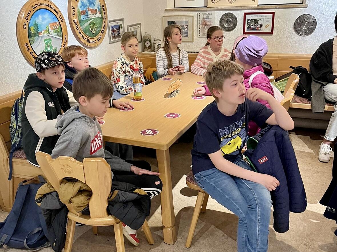 Gruppe von Kindern sitzt an einem Tisch in einem Raum mit Wanddekorationen und bespricht etwas.