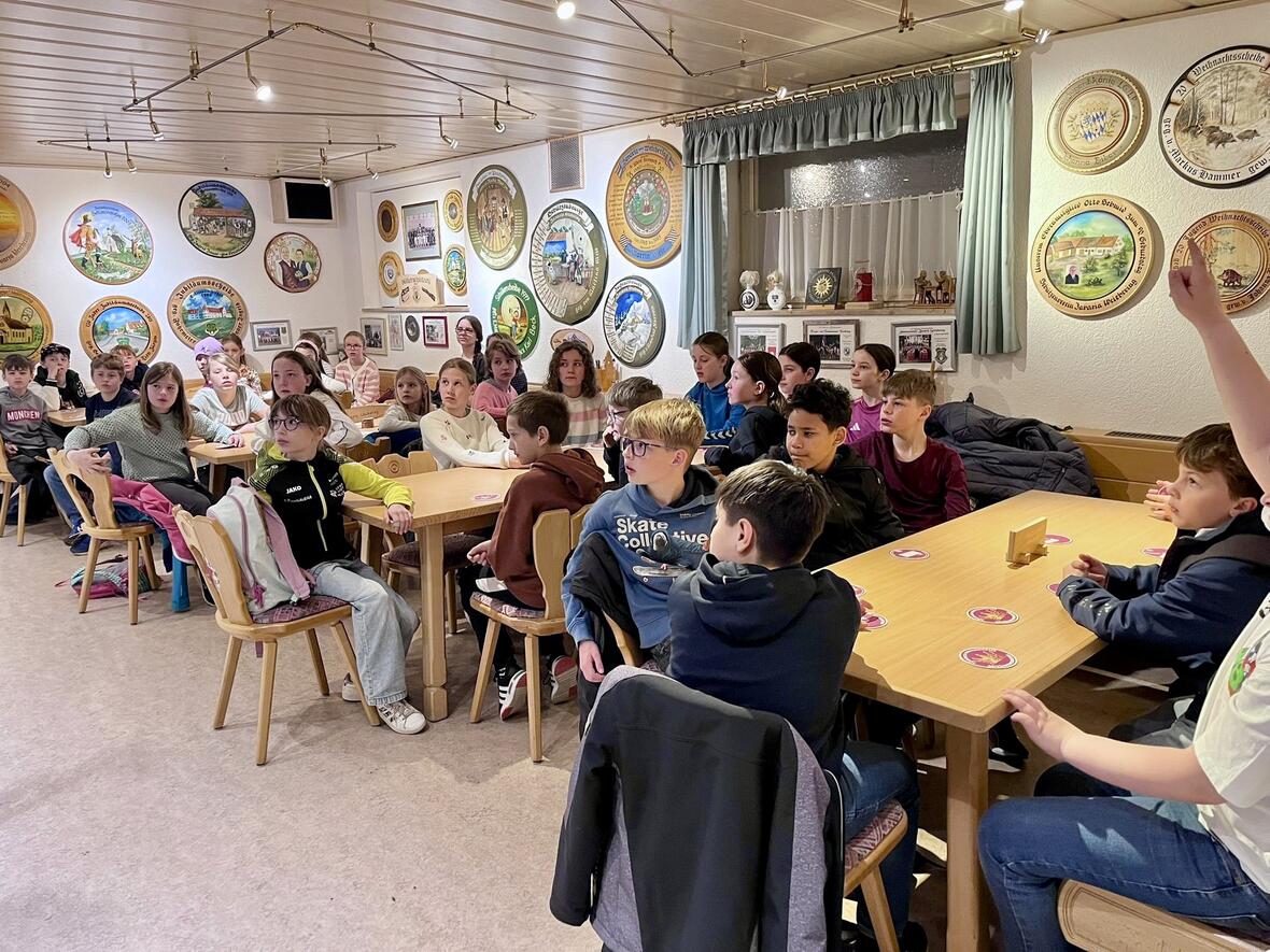 Gruppe von Kindern und Jugendlichen in einem Gasthaus, Zuschauer bei einem Vortrag, viele aufmerksam, einige interagieren.