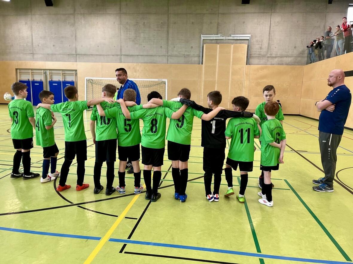 Fußballmannschaft in grünen Trikots bespricht sich vor einem Spiel in der Halle.