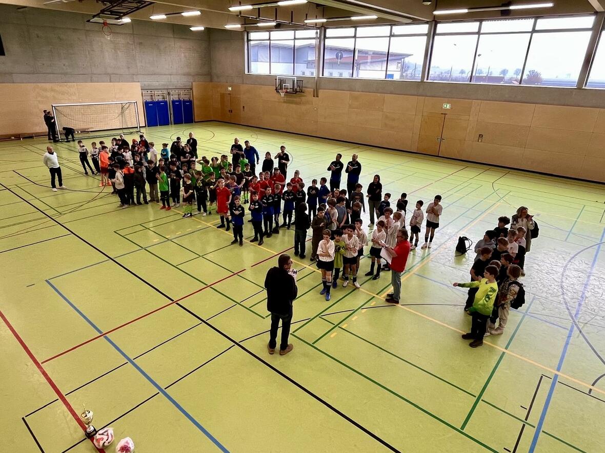 Gruppierung von Kindern in Sportkleidung in einer Halle, während einer Veranstaltung mit einem Redner.