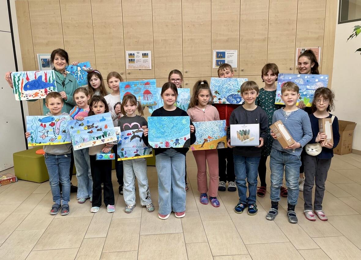 Gruppenbild von Kindern mit ihren bunten Unterwasserzeichnungen in einem hellen Raum.