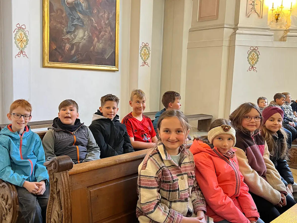 Gruppe von Kindern sitzt in einer Kirche, umgeben von historischen Kunstwerken und Holzbank.