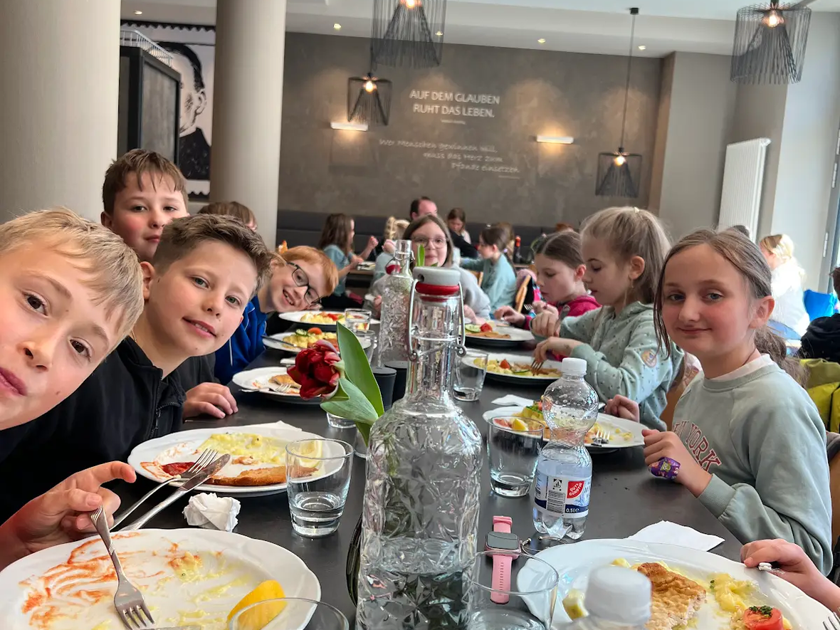 Kinder essen in einem Restaurant, verschiedene Teller mit Essen, frische Blumen auf dem Tisch.