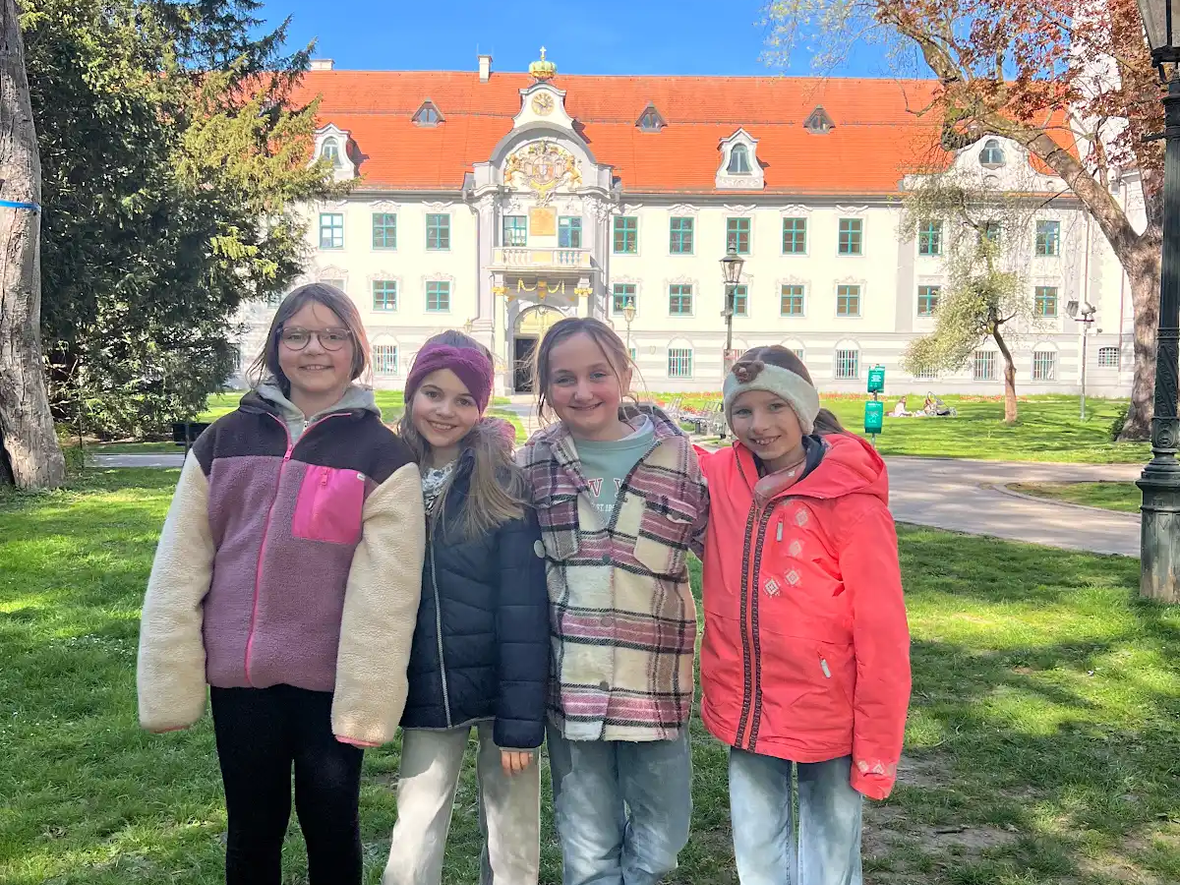 Vier Mädchen stehen vor einem historischen Gebäude im Park bei sonnigem Wetter.
