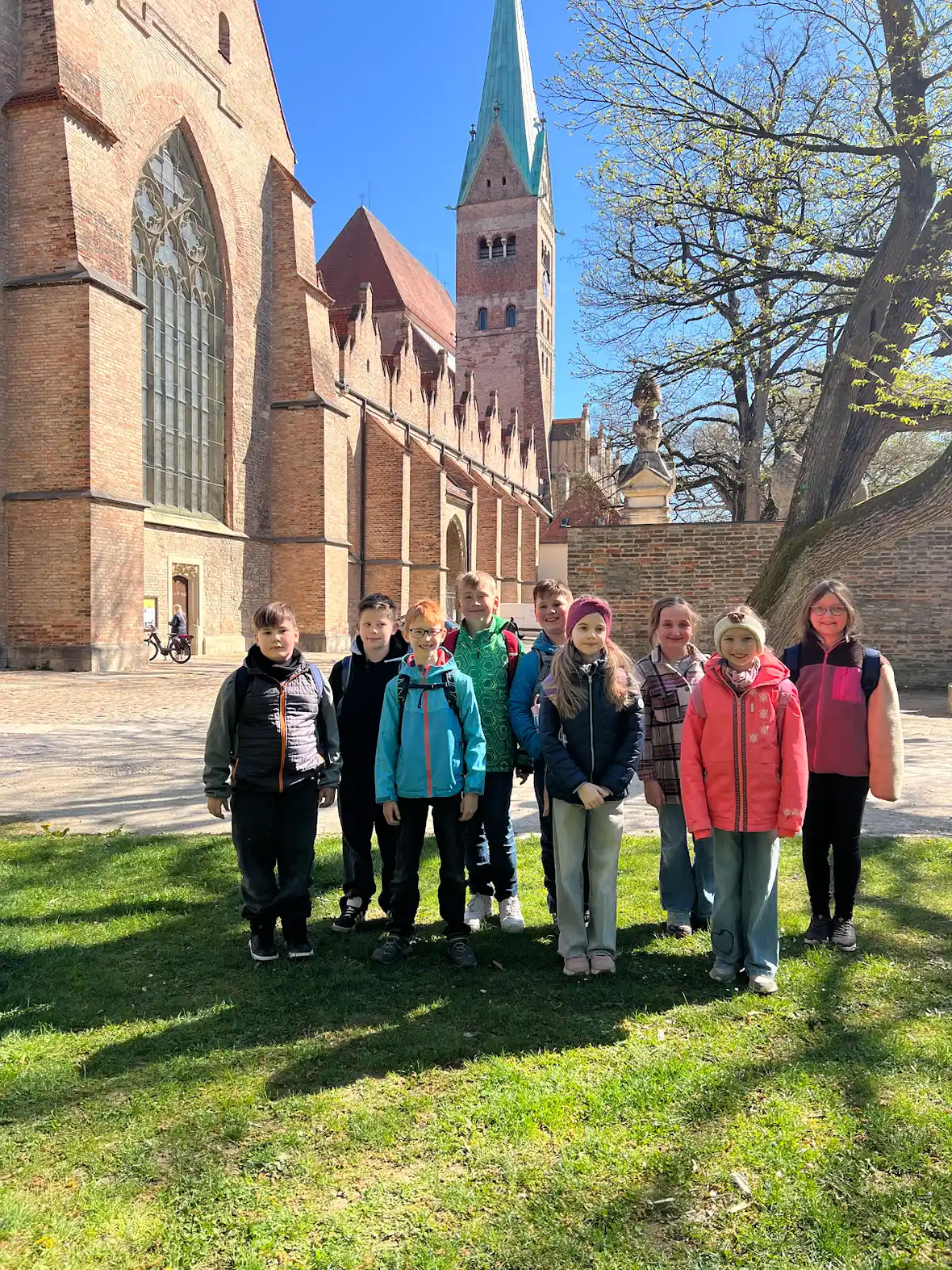 Gruppe von Kindern in einem Park vor einer historischen Kirche mit einem hohen Turm.
