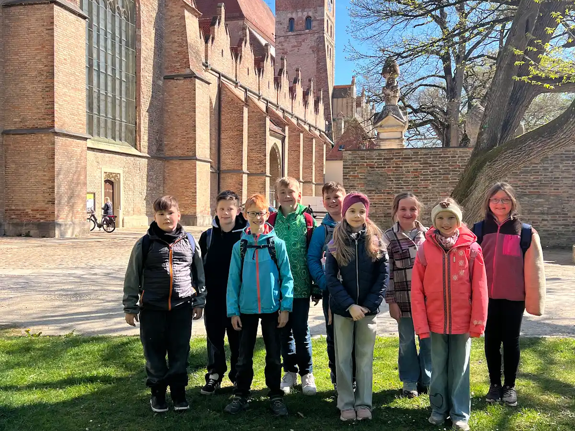 Gruppe von Kindern in einem Park vor einer historischen Kirche mit einem hohen Turm.