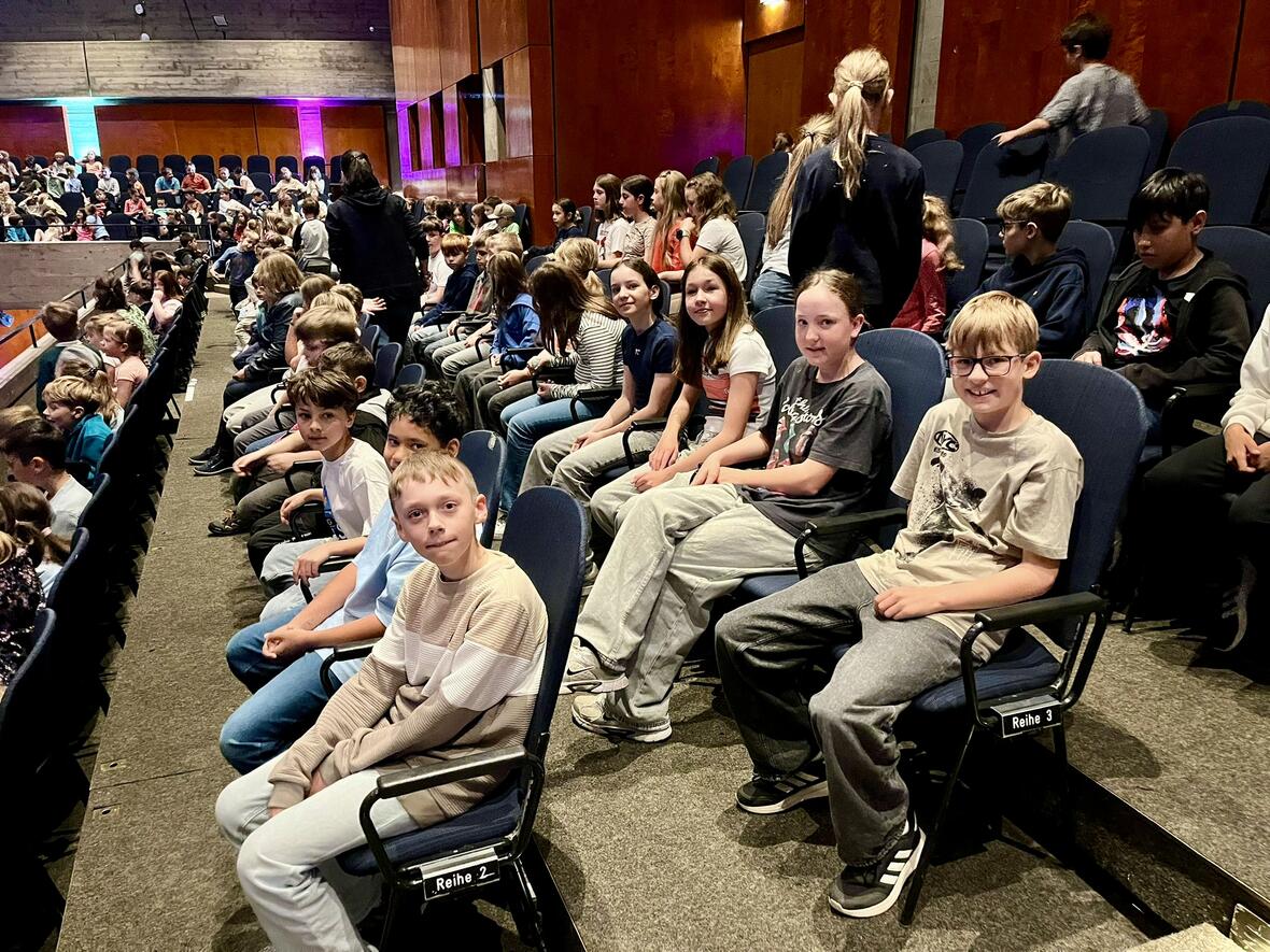 Eine Gruppe von Kindern sitzt im Zuschauerraum eines Theaters, bereit für die Aufführung.