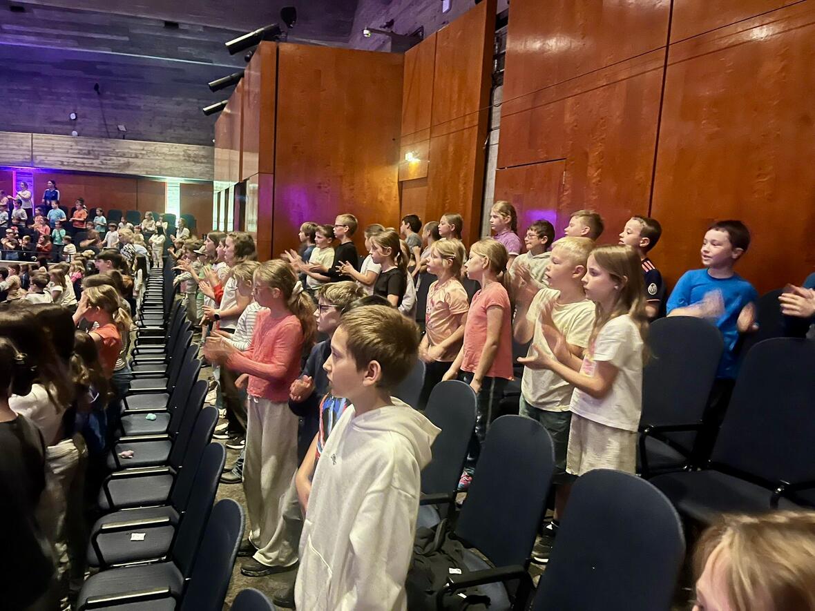 Begeisterte Kinder stehen applaudierend in einem Konzertsaal.