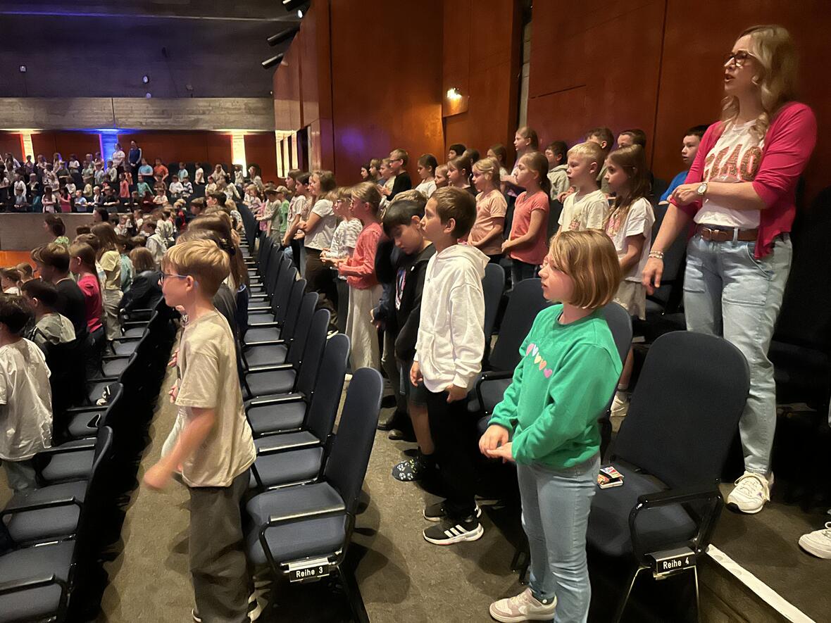 Kinder stehen in einem Saal, einige voller Begeisterung, während andere gespannt zuschauen.
