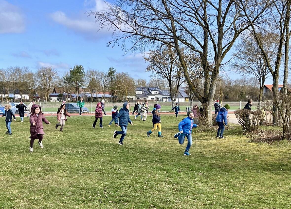 Kinder spielen und rennen fröhlich auf einer Wiese bei sonnigem Wetter.