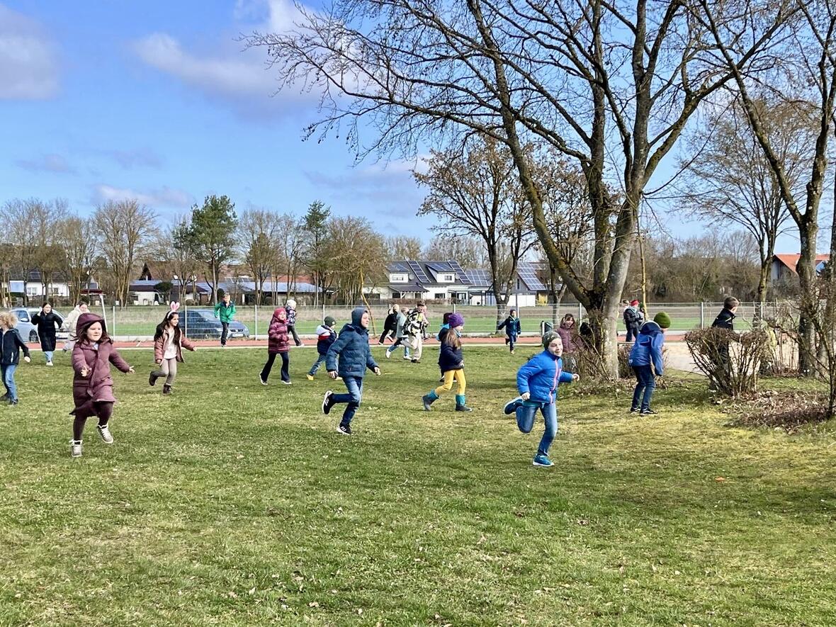 Kinder spielen und rennen fröhlich auf einer Wiese bei sonnigem Wetter.