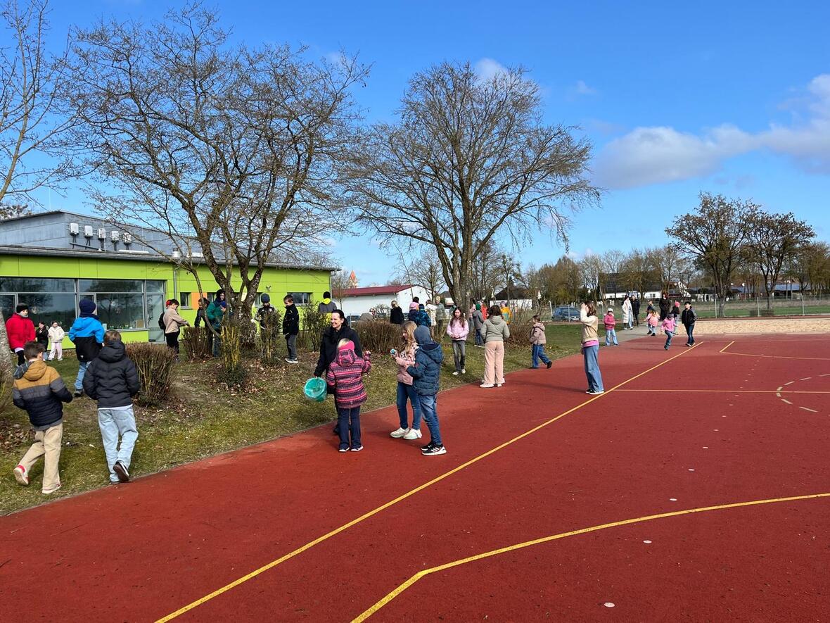 Kinder spielen und stehen auf dem Schulhof neben einem grün gestrichenen Gebäude.