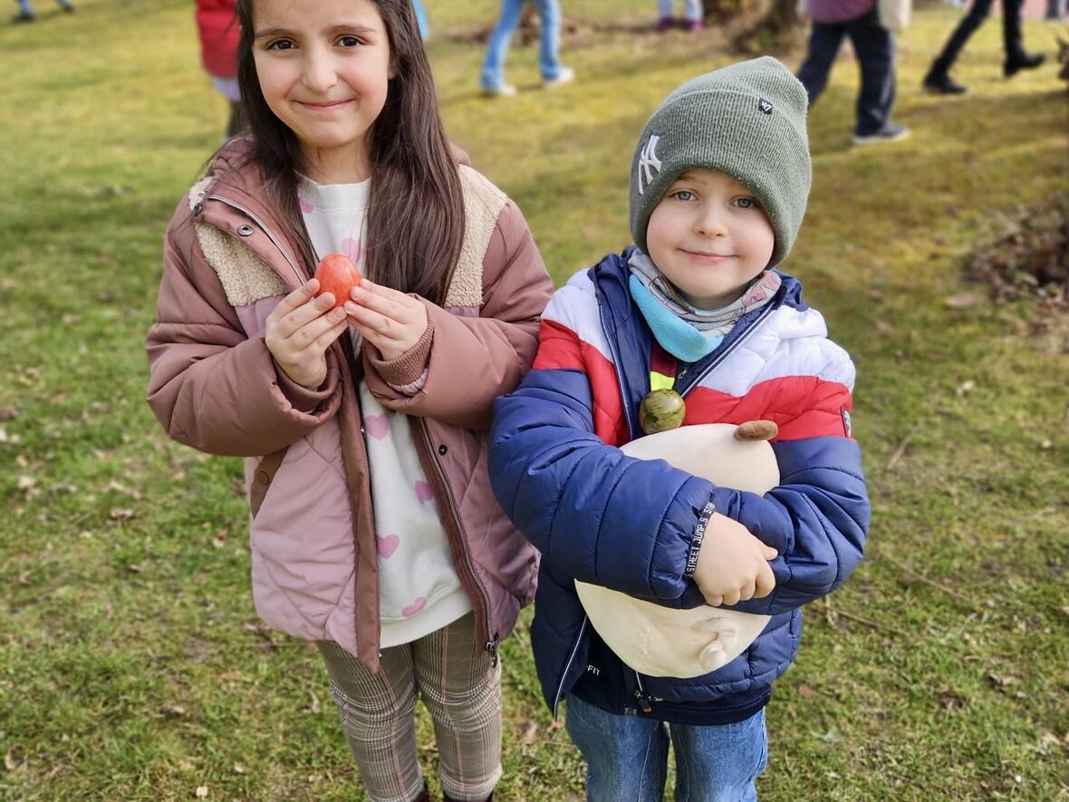 Mädchen mit Hasenohren und Junge in Mütze halten Eier im Park während einer Osterveranstaltung.